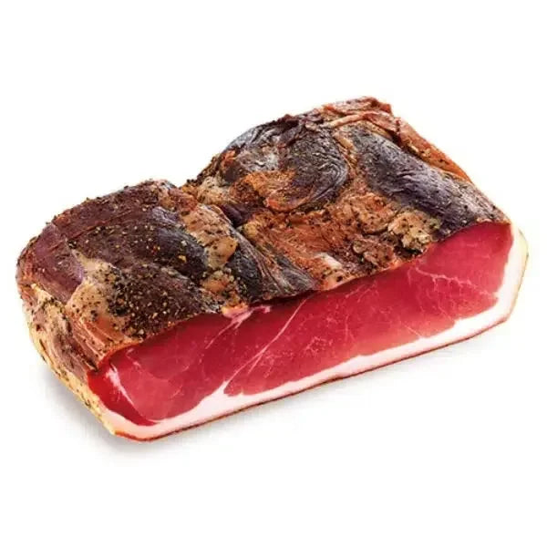 Close-up of a cured speck meat piece with a dark seasoned crust and deep red interior on white background