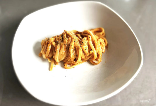 Red roasted pepper pesto linguine garnished with black pepper in a white bowl